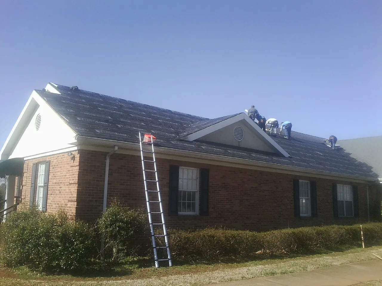 Crew tearing shingles off a brick ranch roof with a ladder set — Metal Roof Repair work by our crew in Kandiyohi