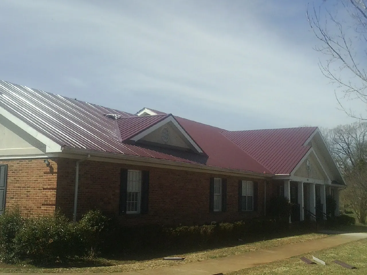 Red metal roof with gabled entries on a long brick building, from a Hail Damage Roof Repair job in Kandiyohi