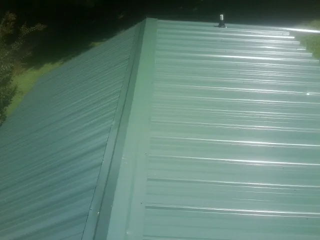 New green metal panels meeting at the ridge of a roof — Flat Roof Repair work by our crew in Kandiyohi