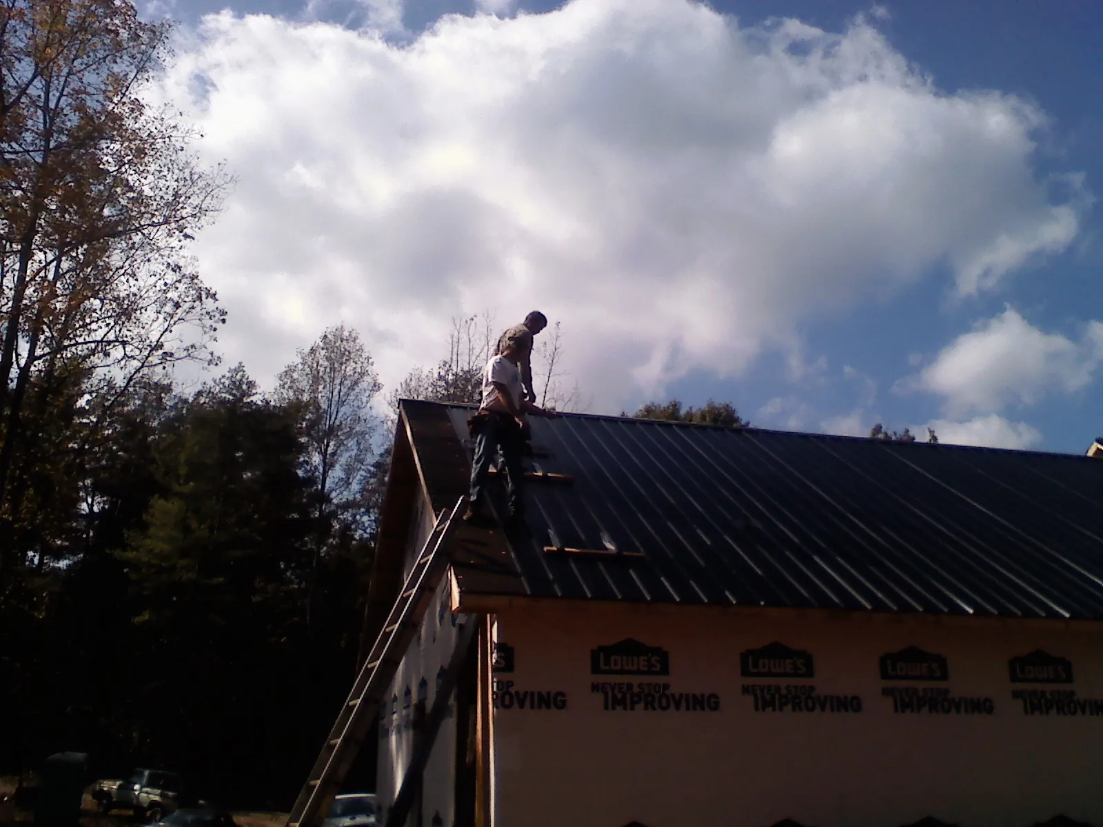 Roofer fastening dark metal panels high against a cloudy sky, from a Roof Inspection job in Kandiyohi