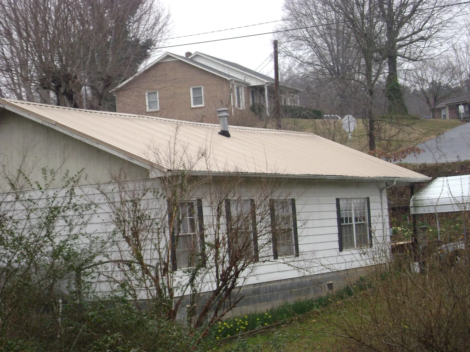 Tan metal roof on a white sided house set into a hillside — Commercial Roofing by Roofing Brothers in Kandiyohi